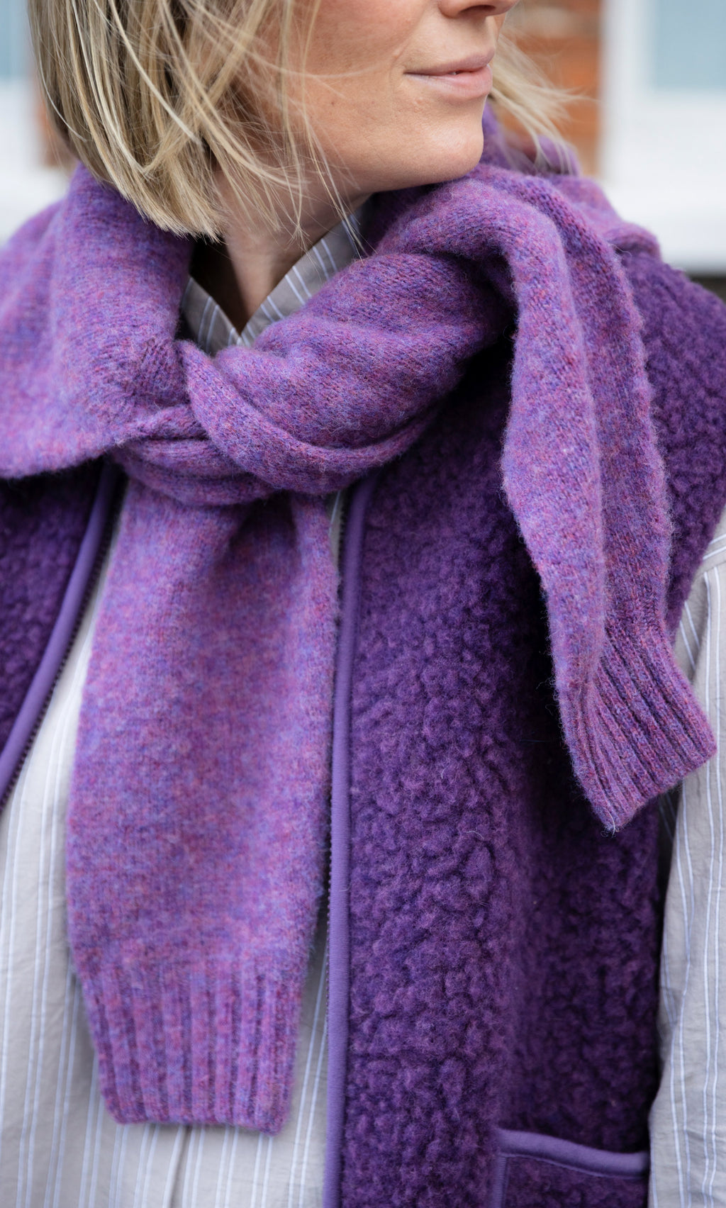 Plümo  A person wearing a purple textured Irish wool Maylin Gilet with a matching heather knit scarf draped over their shoulders.