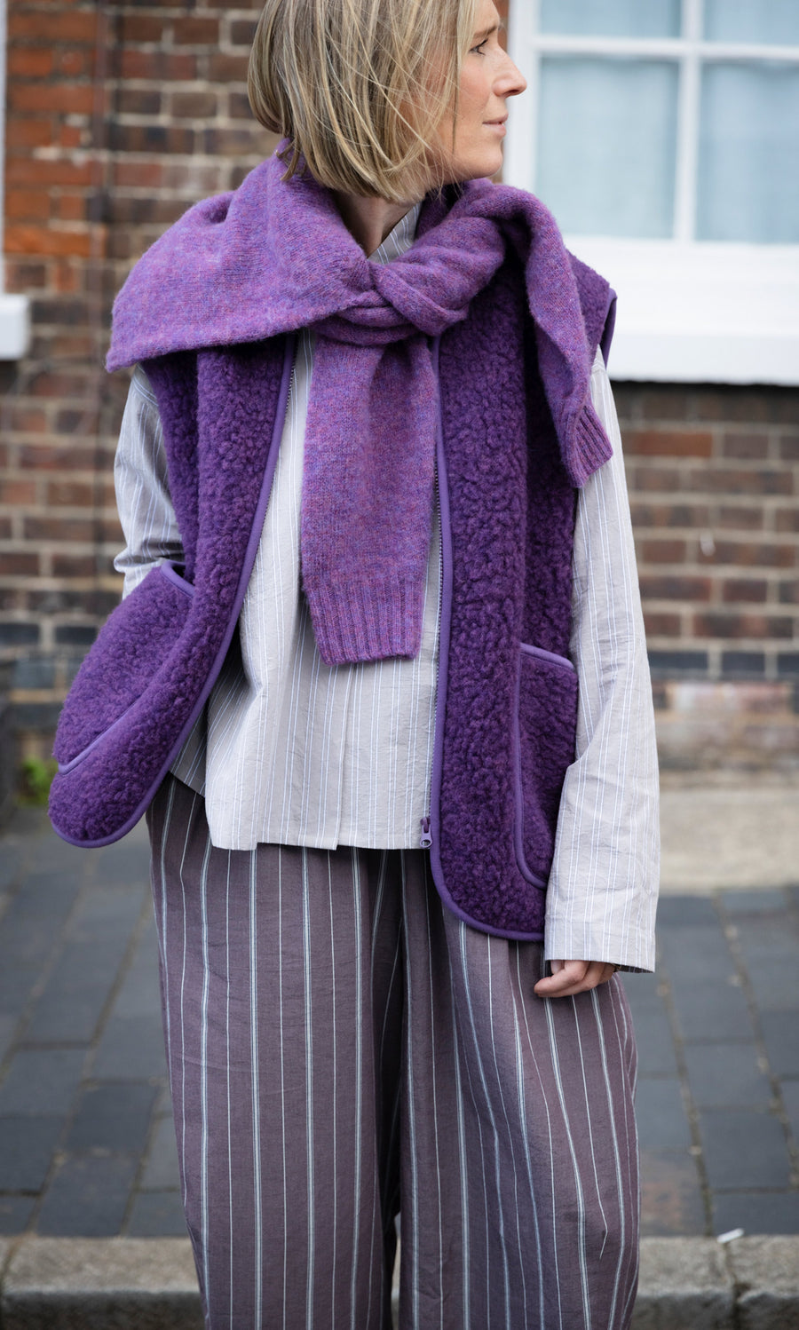 Plümo  A person wearing a cropped, heather purple Maylin Gilet over a matching sweater, striped shirt, and striped pants.