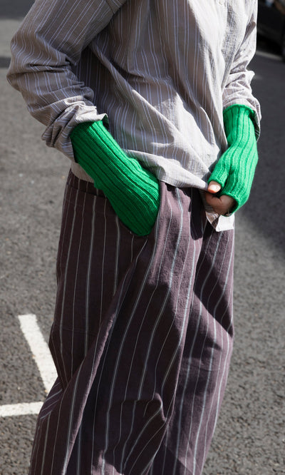 Plümo  A person wearing vibrant green Green Wristwarmers, featuring a fingerless, ribbed design.