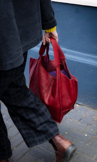 Plümo  A person walking while carrying a large, red leather Miller Bag - Burnt Sienna hobo bag.