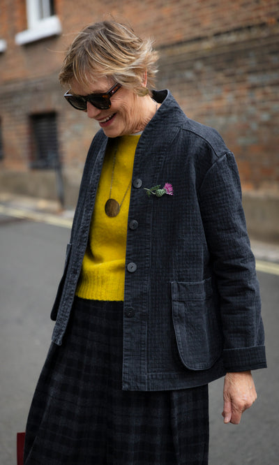 Plümo  Woman wearing a coal Envoy Jacket over a yellow sweater and a plaid skirt.