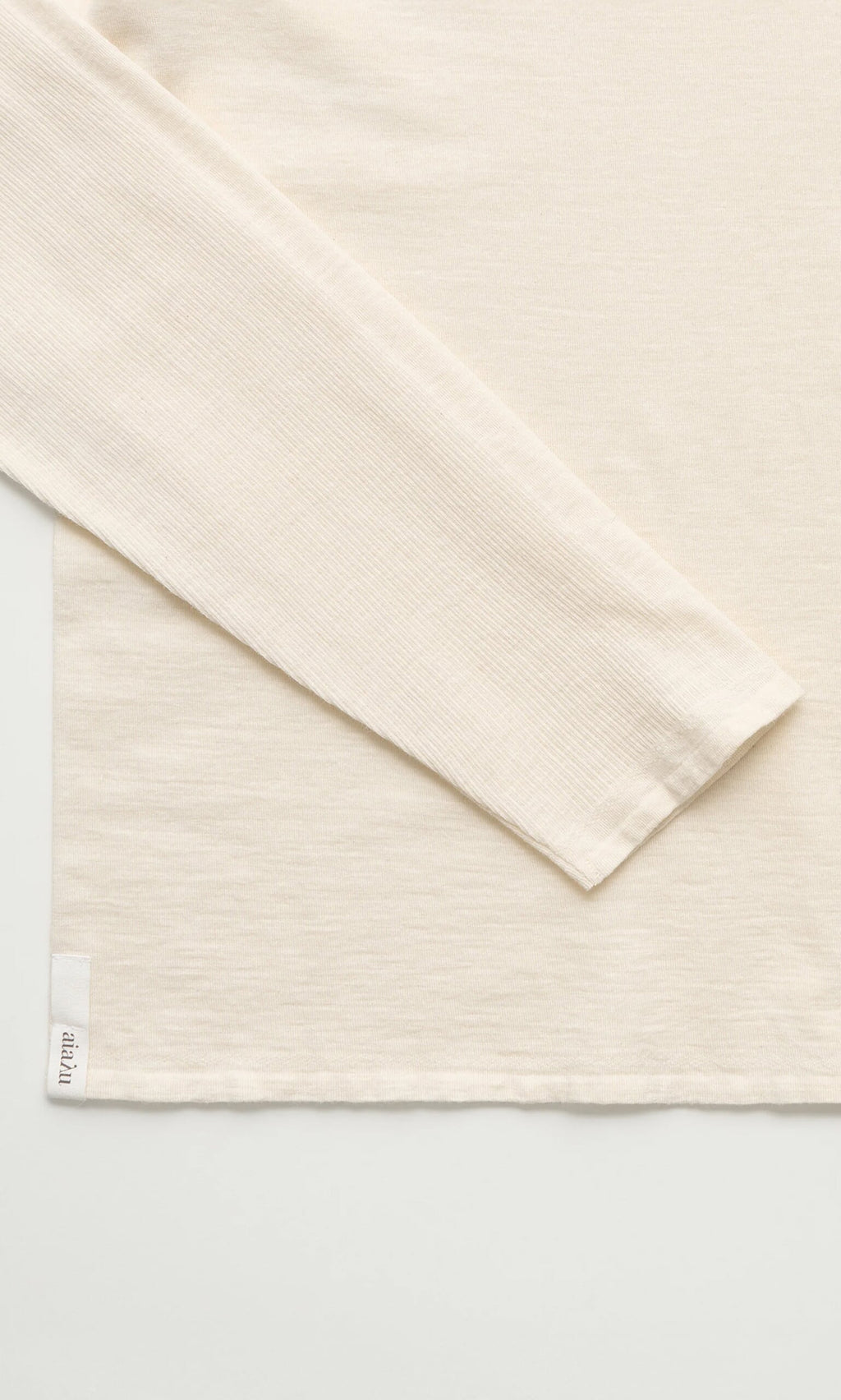 Plümo- A close-up of the Gentle Turtleneck in cream cotton-cashmere, featuring a small white hem tag.