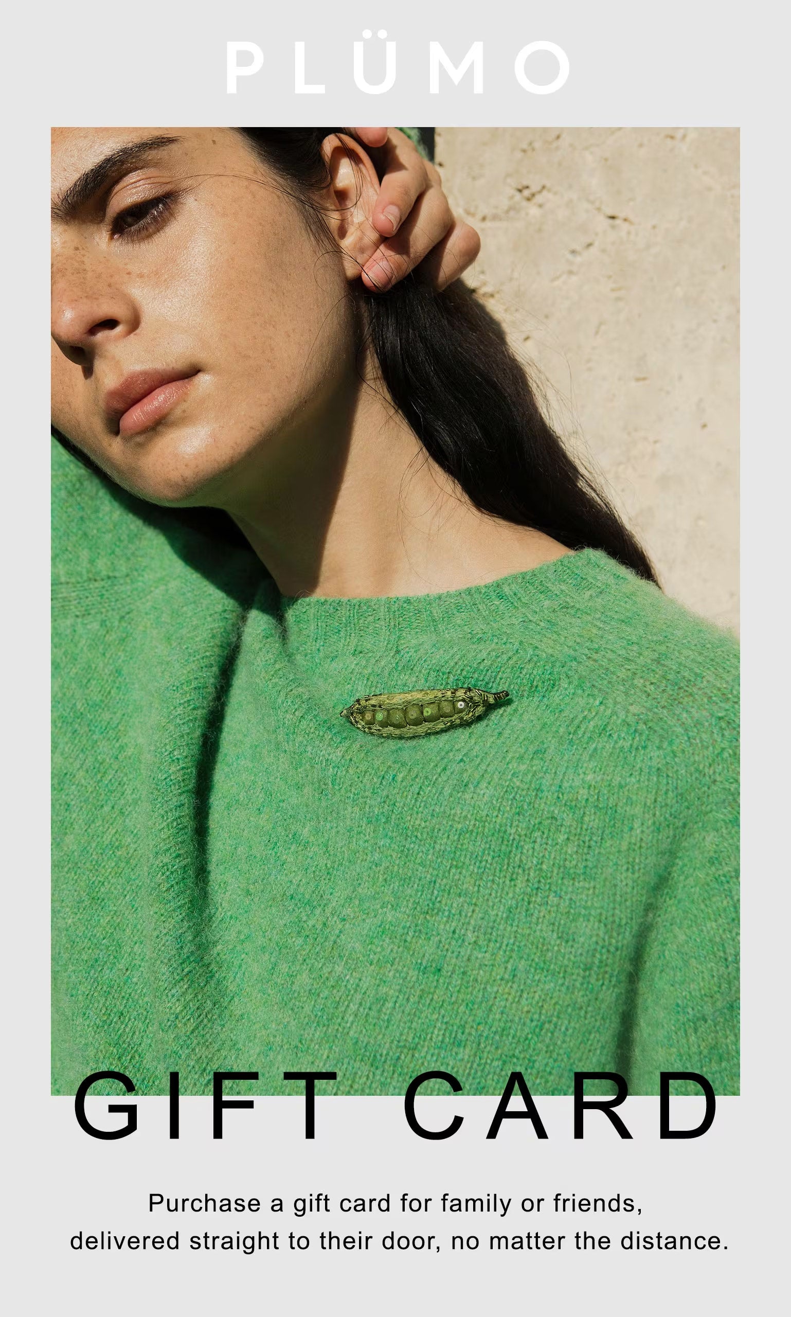 Plümo Woman in a green sweater by a textured wall, highlighting the Plümo Gift Card as the perfect physical gift.