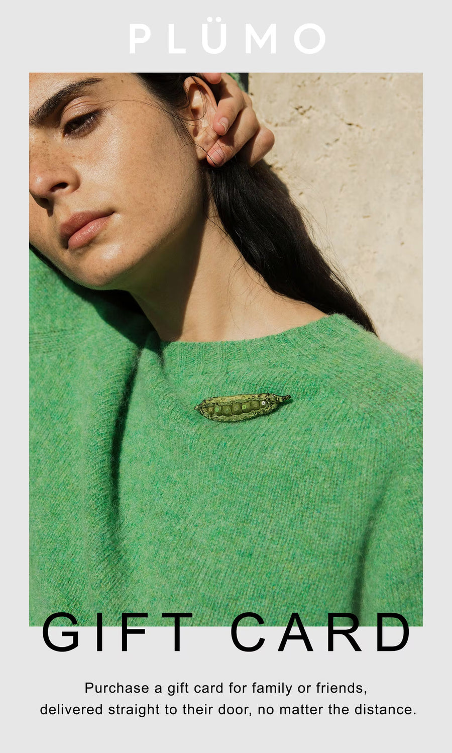Plümo Woman in a green sweater by a textured wall, highlighting the Plümo Gift Card as the perfect physical gift.