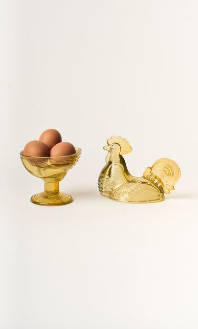 Plümo- A Glass Hen Bowl holds brown eggs next to a matching storage container on a white background.