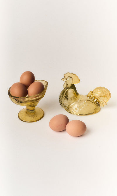 Plümo- Glass Hen Bowl with brown eggs, chicken-shaped dish, and two eggs on a white background.