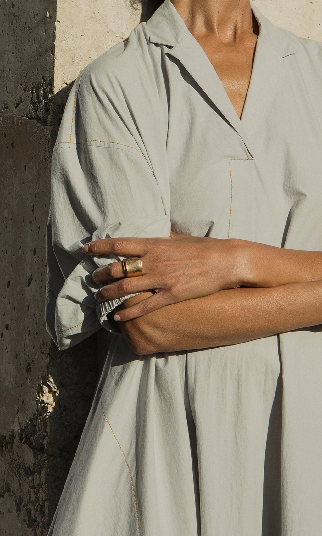 Plümo- A person in a light, loose dress stands by a stone wall, arms folded, wearing the handcrafted Lucca Ring.