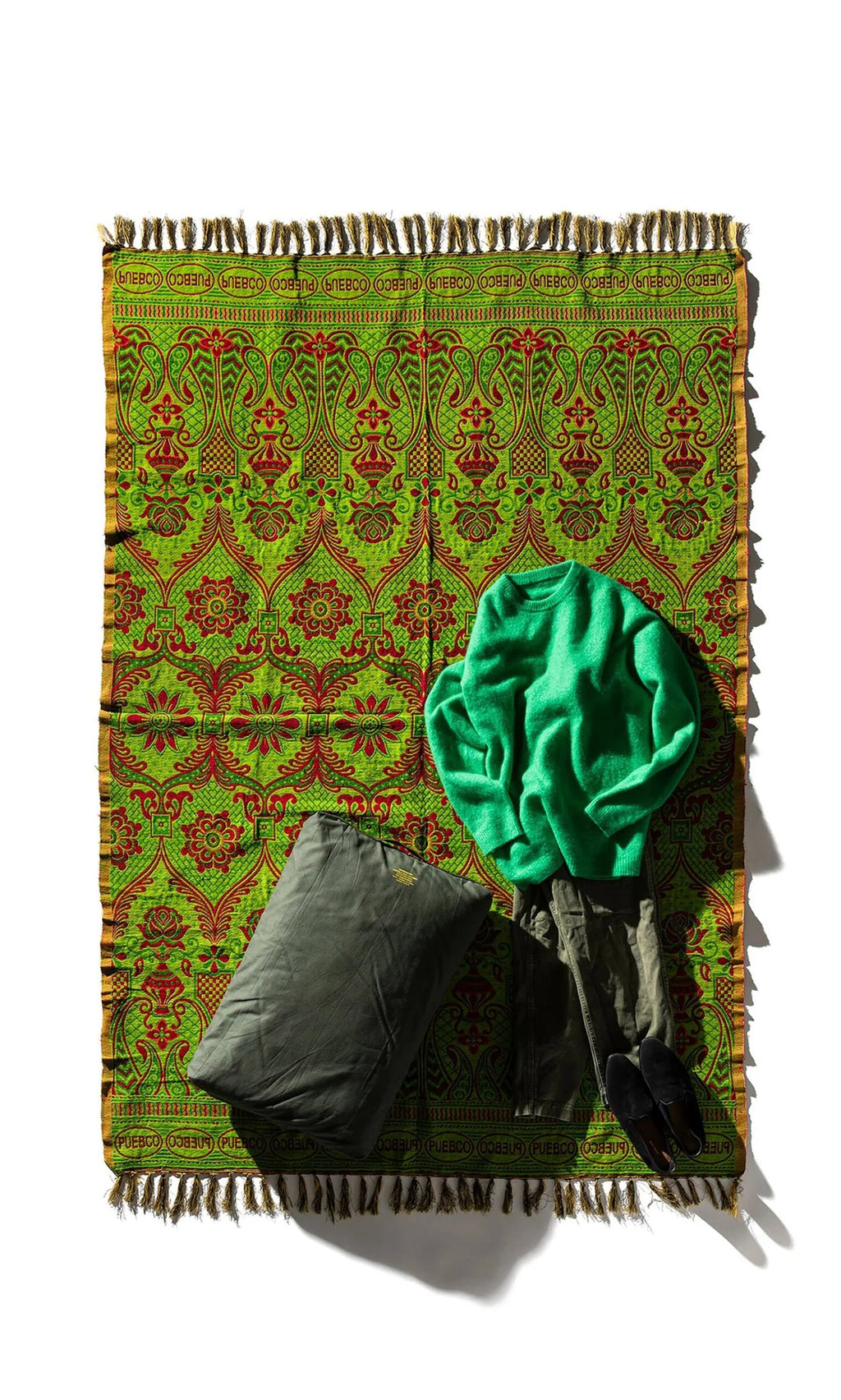 Plümo- A Green Jacquard Rug topped with a green sweater, gray pants, and a gray pillow.