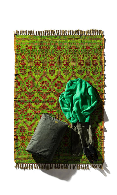 Plümo- A Green Jacquard Rug topped with a green sweater, gray pants, and a gray pillow.
