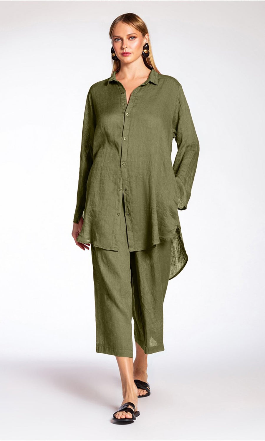 Plümo- Woman wearing Lumira Linen Pants in olive green with a matching button-up top and black sandals, walking forward.