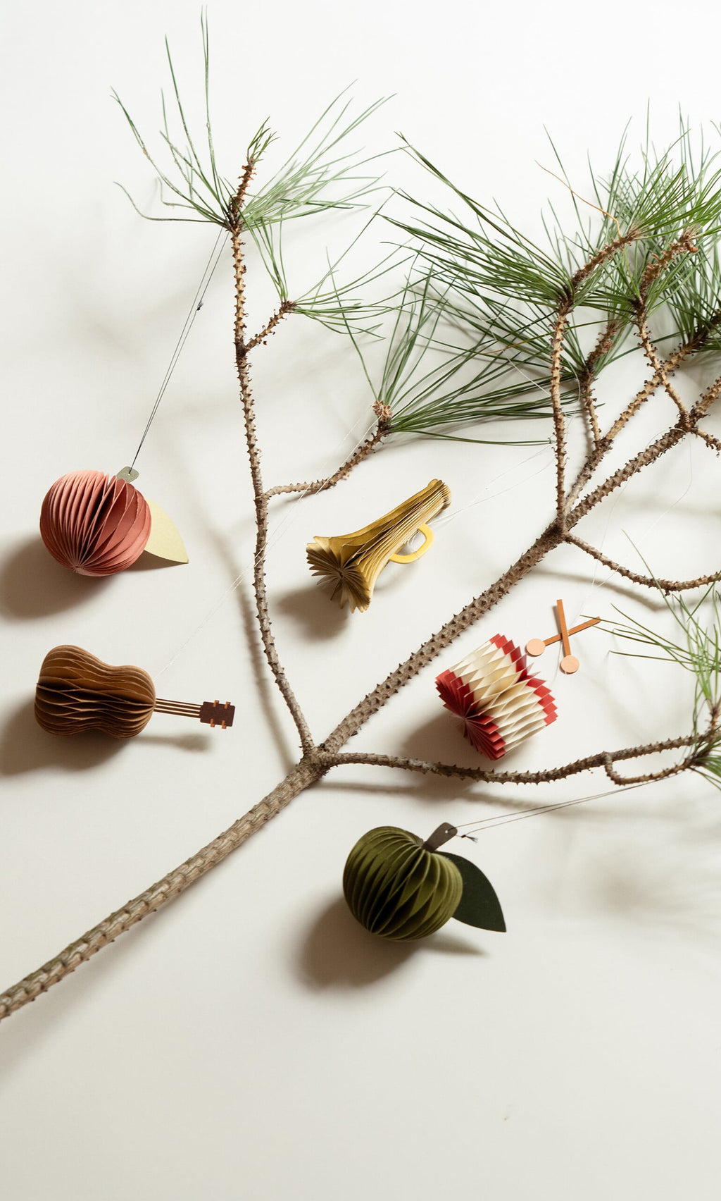 Plümo- A pine branch with Honeycomb Apples (set of 2) and paper ornaments on a white background.