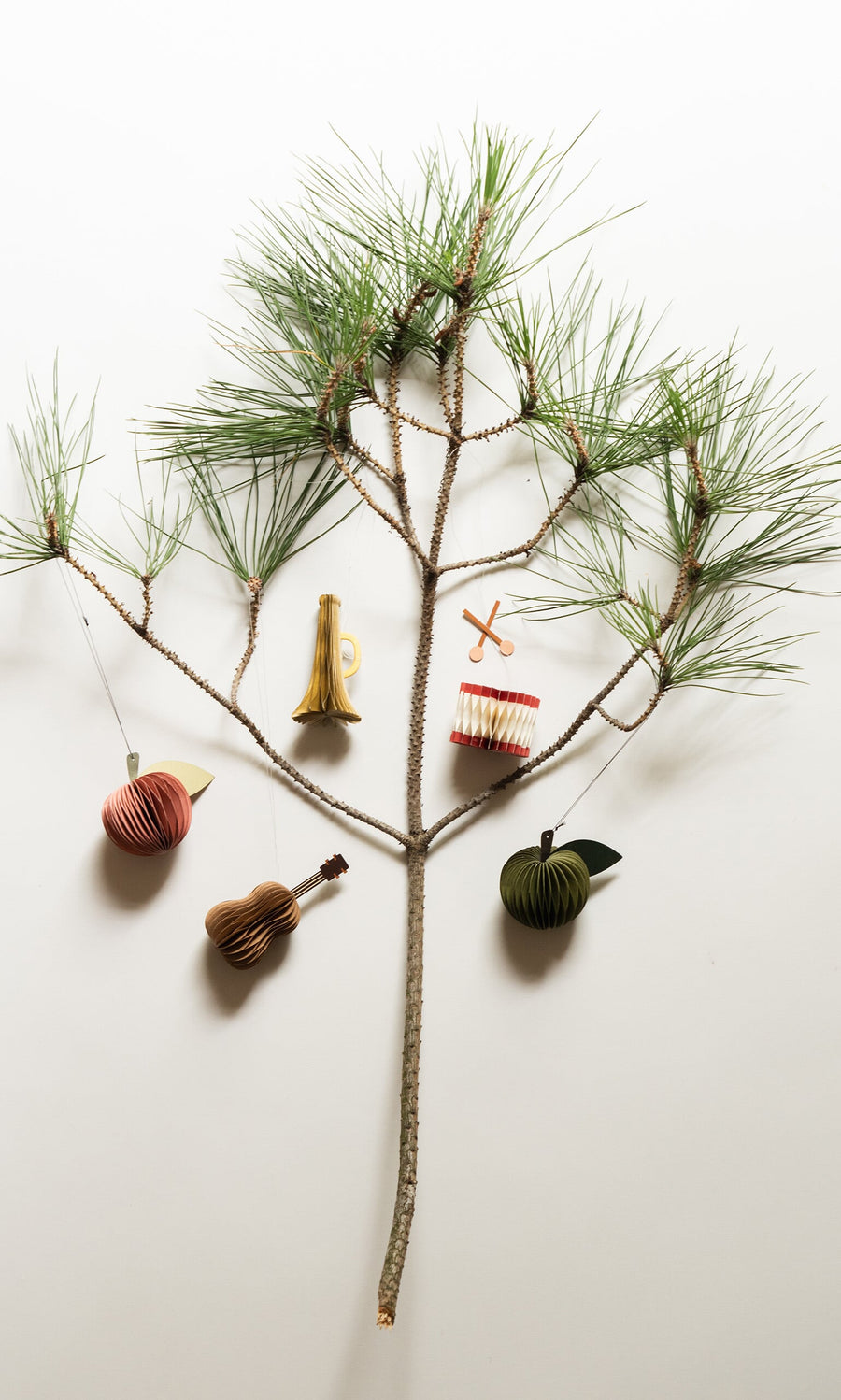Plümo- A pine branch adorned with Christmas ornaments: Honeycomb Instruments (set of 3), propeller, apple, and green fruit.