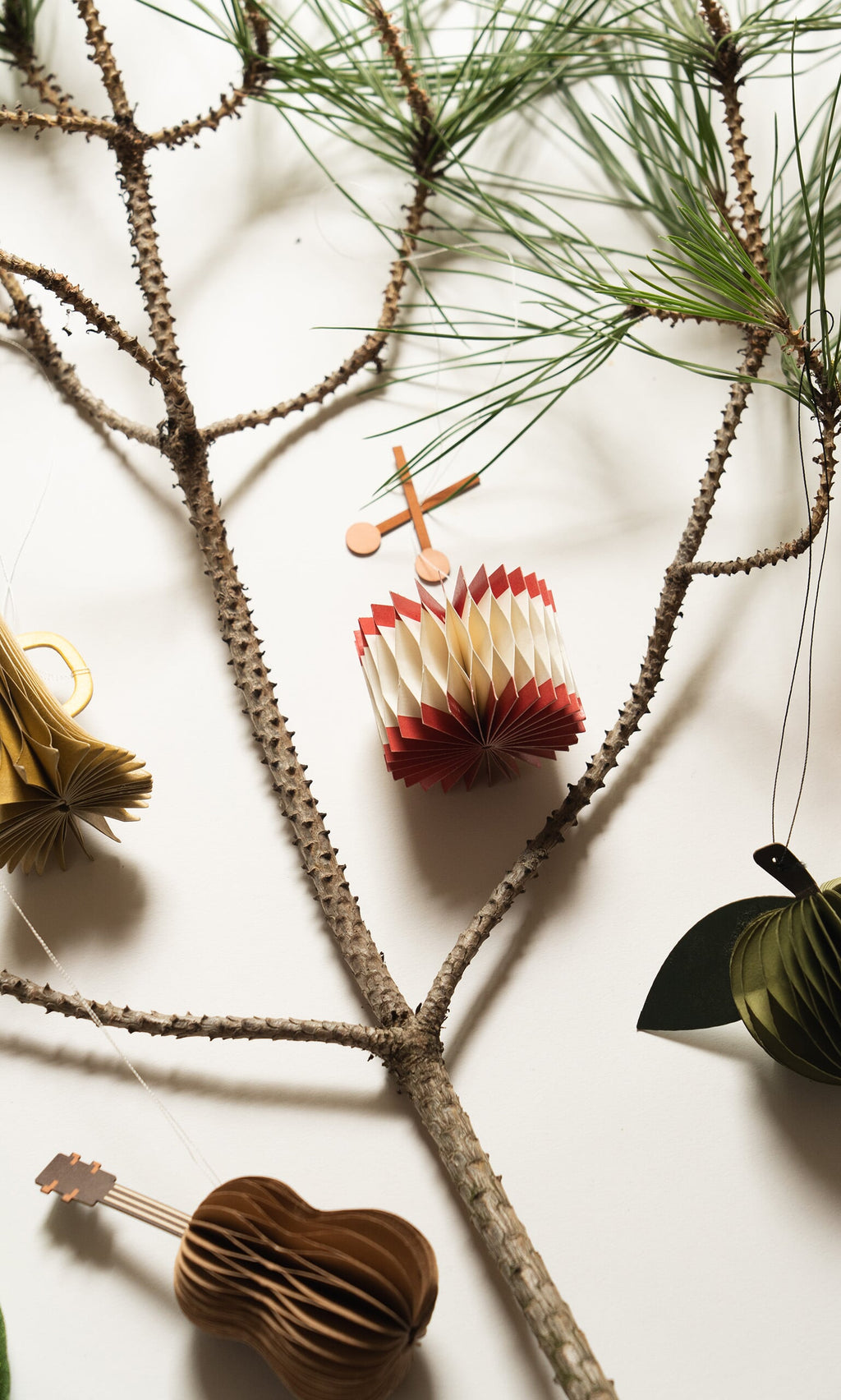 Plümo- A pine branch with Honeycomb Instruments (set of 3) ornaments—drum, guitar, and fruit—on a white background.