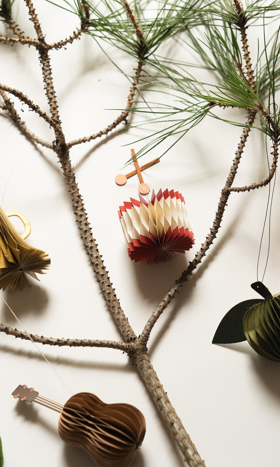 Plümo- A pine branch with Honeycomb Instruments (set of 3) ornaments—drum, guitar, and fruit—on a white background.