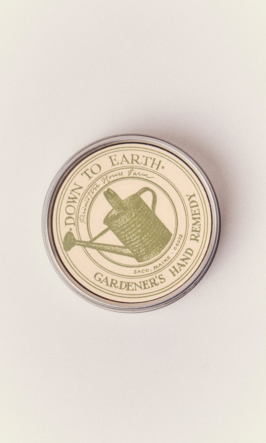 Plümo- Round tin labeled Gardener's Hand Remedy, a nourishing hand balm with herbal ingredients and a green watering can.