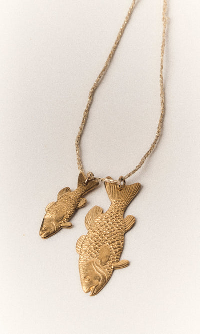 Plümo- The Kala Necklace features two gold-plated fish pendants on an adjustable chain, displayed on a light background.