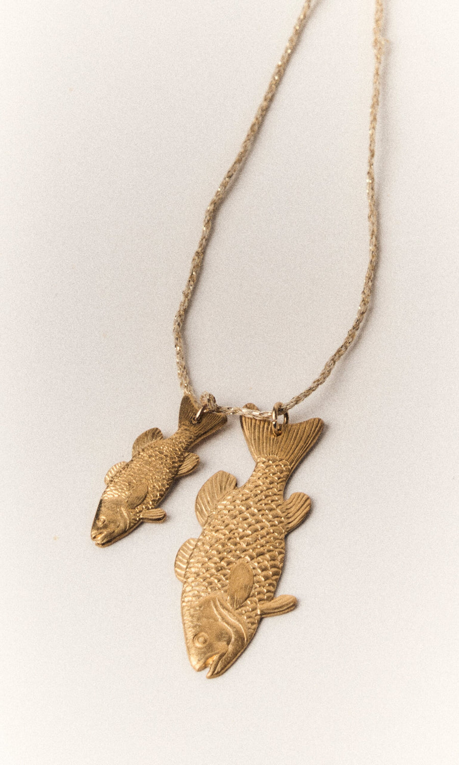 Plümo- The Kala Necklace features two gold-plated fish pendants on an adjustable chain, displayed on a light background.