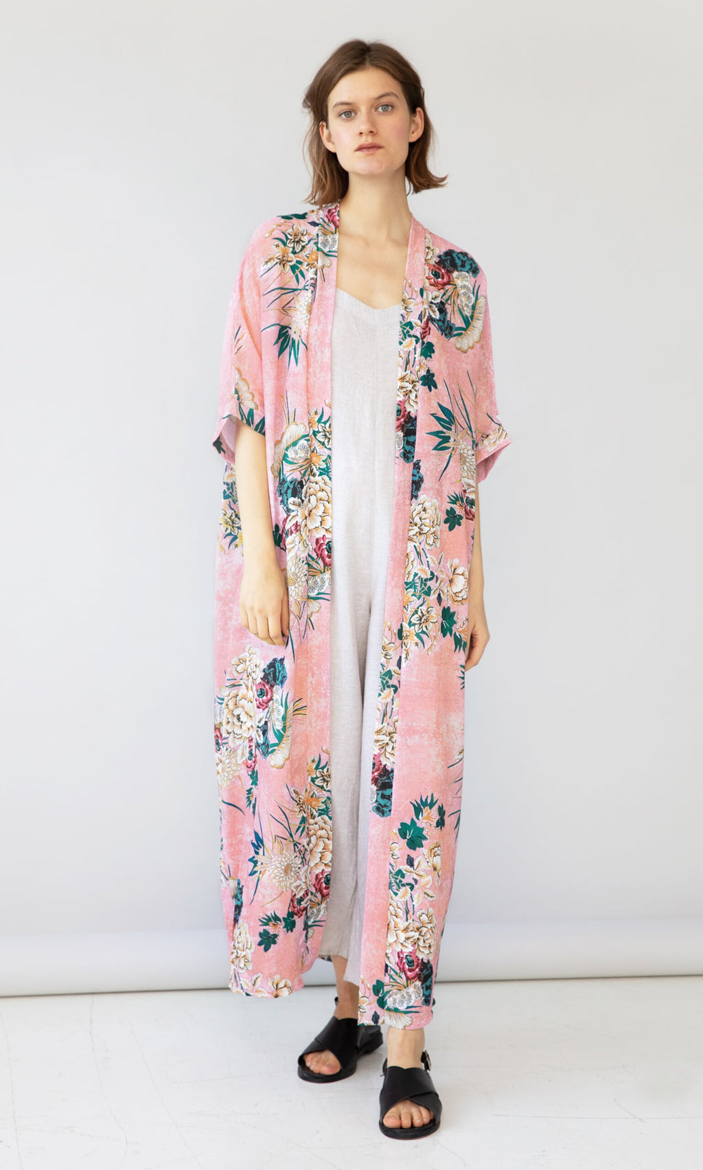 Plümo- Woman models the Tarifa Kimono, a long floral print layer, over a white dress against a light background.