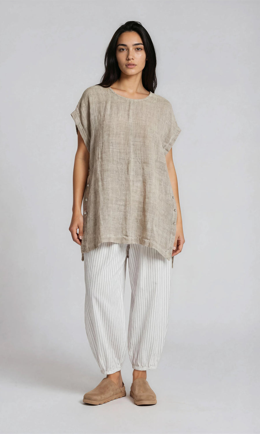 Plümo- Woman wears the Kostas Blouse with white pinstriped pants and tan slip-ons, standing against a light background.