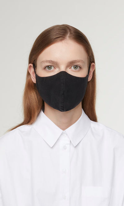 Plümo  Person with long brown hair in a white shirt wears the Organic Linen Mask - Black, looking directly at the camera.