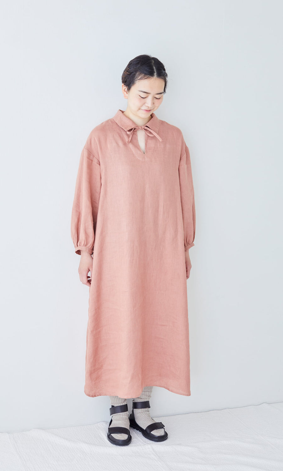 Plümo- A person stands against a white background, wearing a pink dress, Linen Rib Socks, and black sandals.