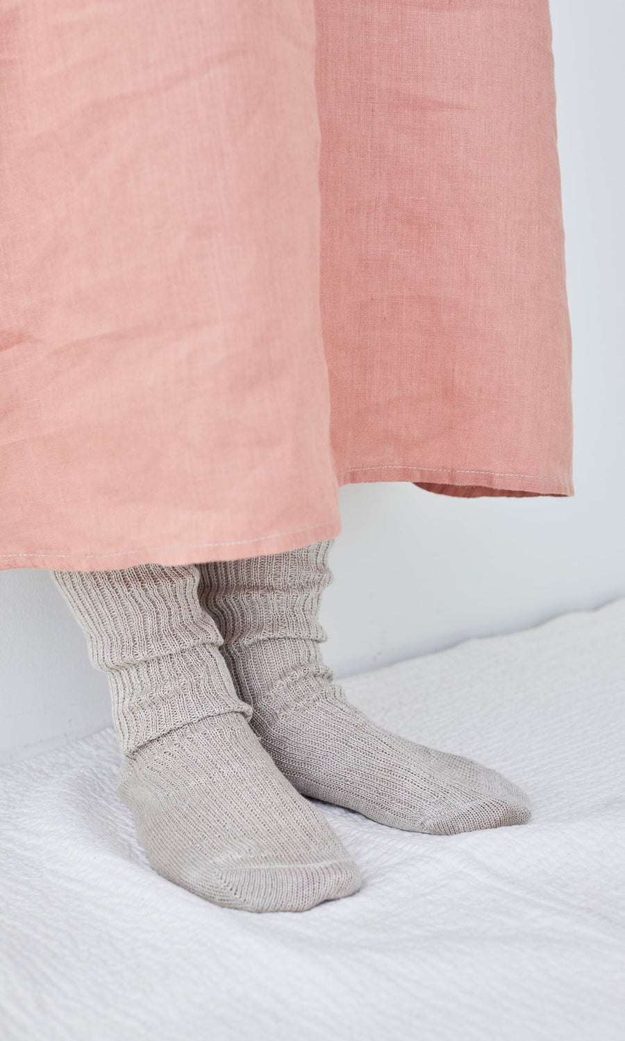 Plümo- Person wearing Linen Rib Socks and a long pink skirt, standing on a white textured surface against a white wall.
