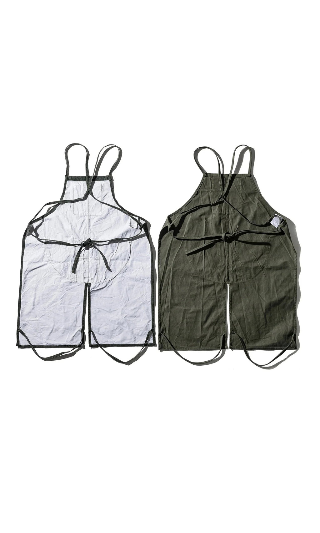 Plümo- Two Lumberjack Aprons, sleeveless with black straps, in dark green fabric, laid flat side by side.