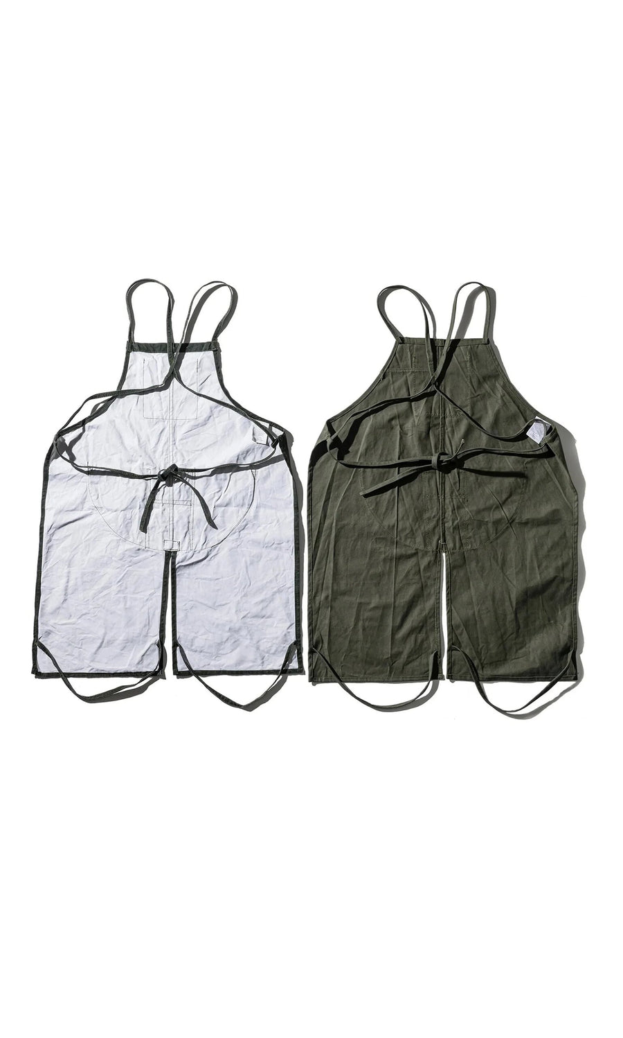 Plümo- Two Lumberjack Aprons, sleeveless with black straps, in dark green fabric, laid flat side by side.