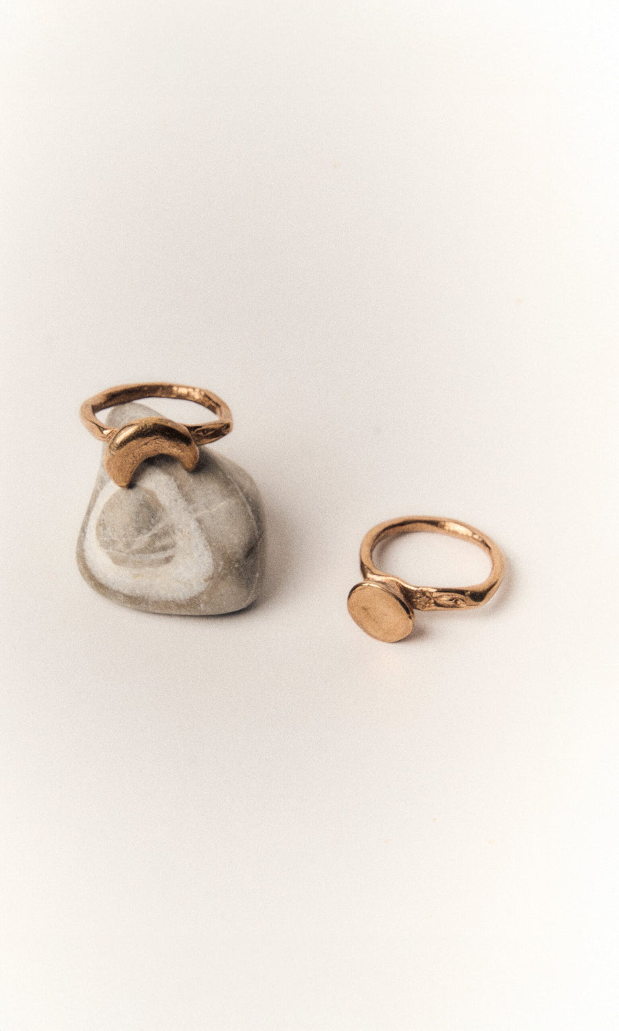 Plümo- The Moon Circle Stacking Ring—one atop a gray stone with white markings, another flat on a white surface.