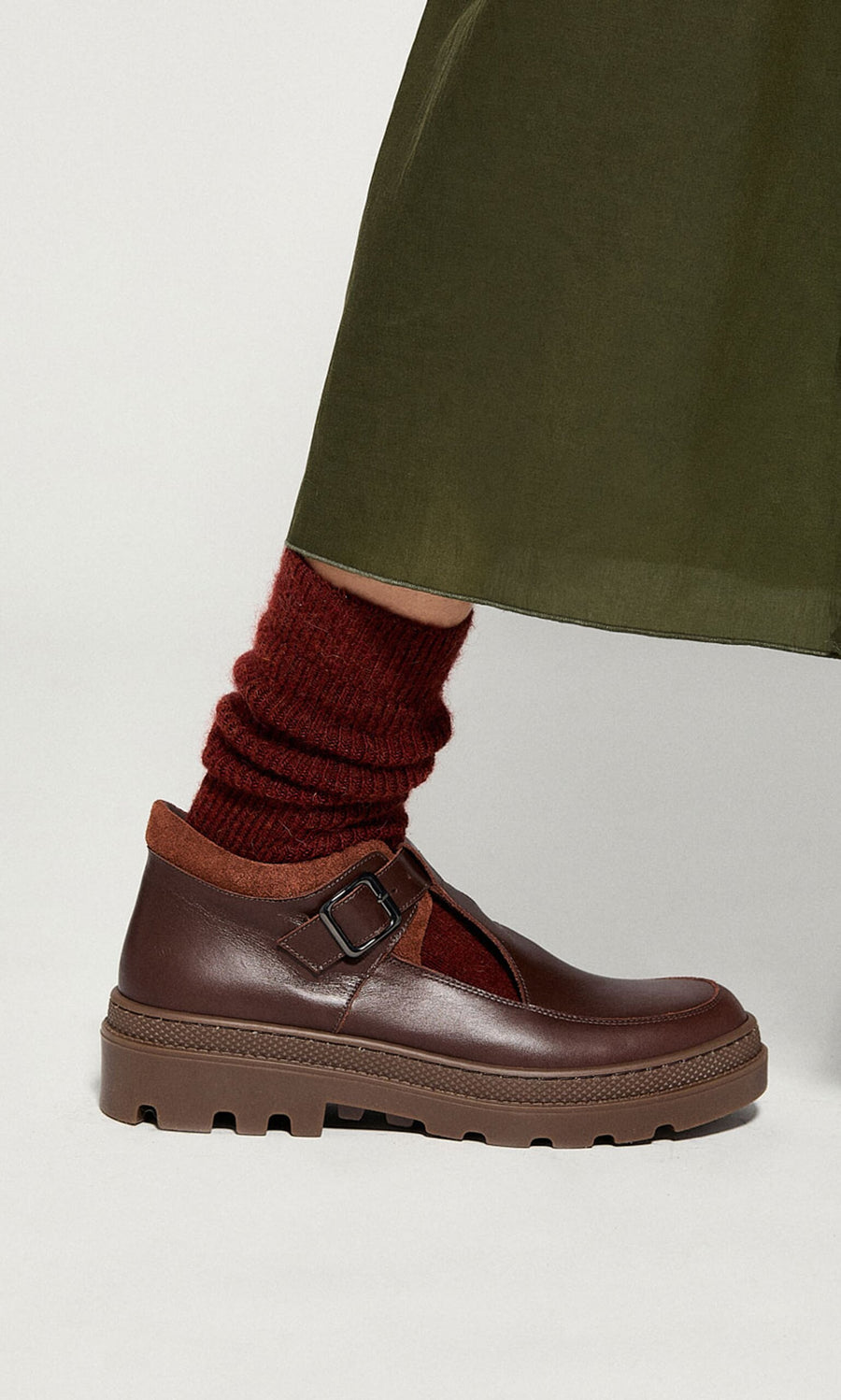 Plümo- Someone in a dark green skirt, red socks, and brown Toba Shoes with rubber soles and a buckle.