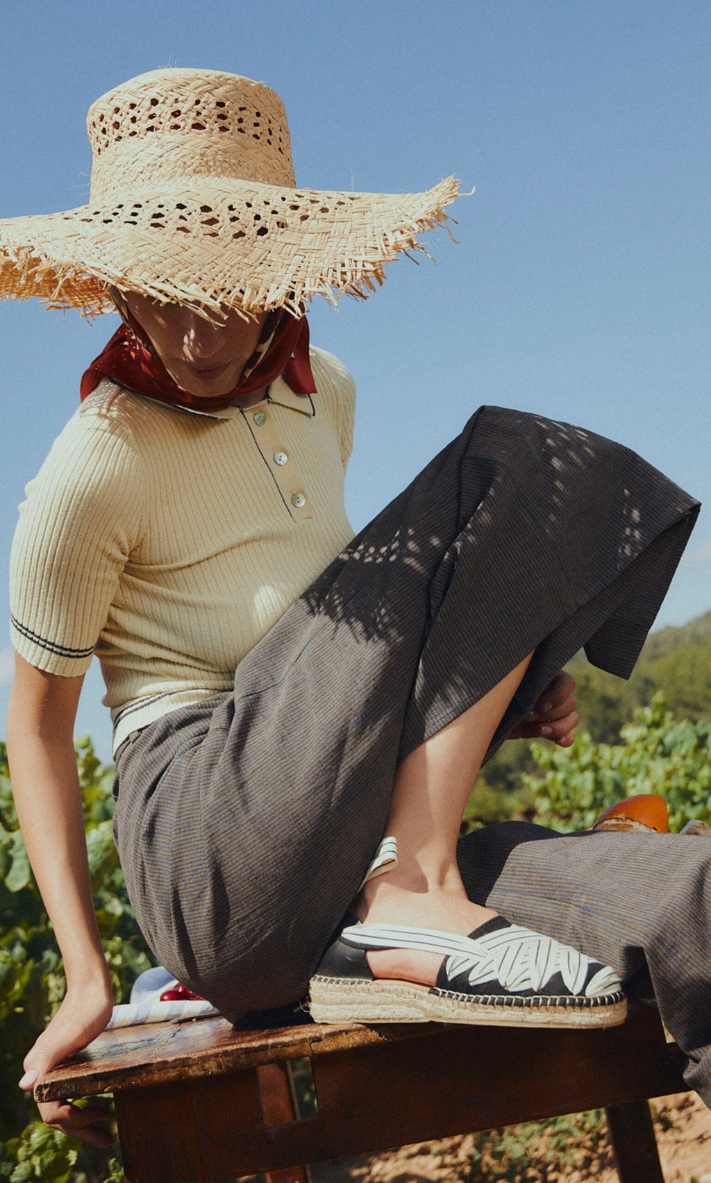 Plümo- A person in a straw hat and cream shirt sits outdoors, one leg up, wearing chic Ribbon Espadrilles with a jute wedge.