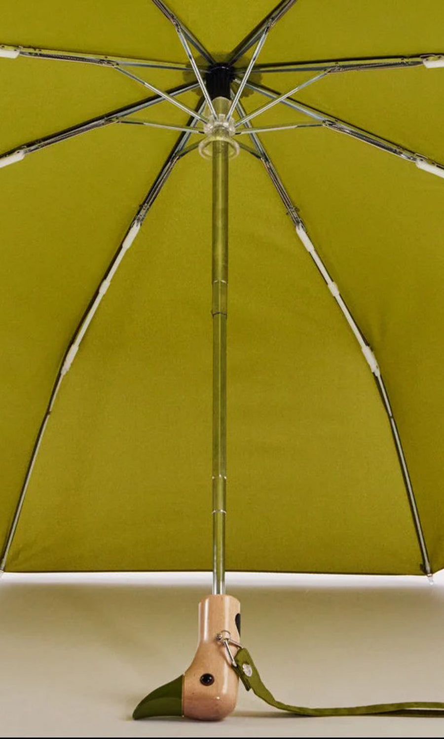 Plümo  Duck Umbrella - Olive: Compact metal-frame umbrella, upright on beige surface; handle at bottom.
