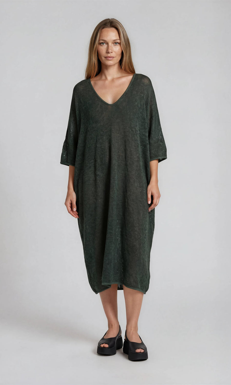 Plümo- A woman wears the Opema Kaftan and black platform sandals, standing against a light grey background.