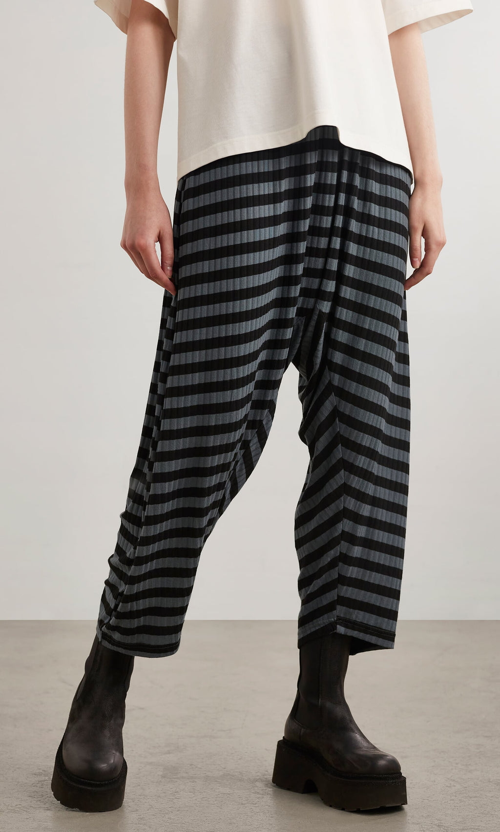 Plümo- Person wearing Oyster Catcher Pants - Grey Stripe with a white top and black platform boots on a gray floor.