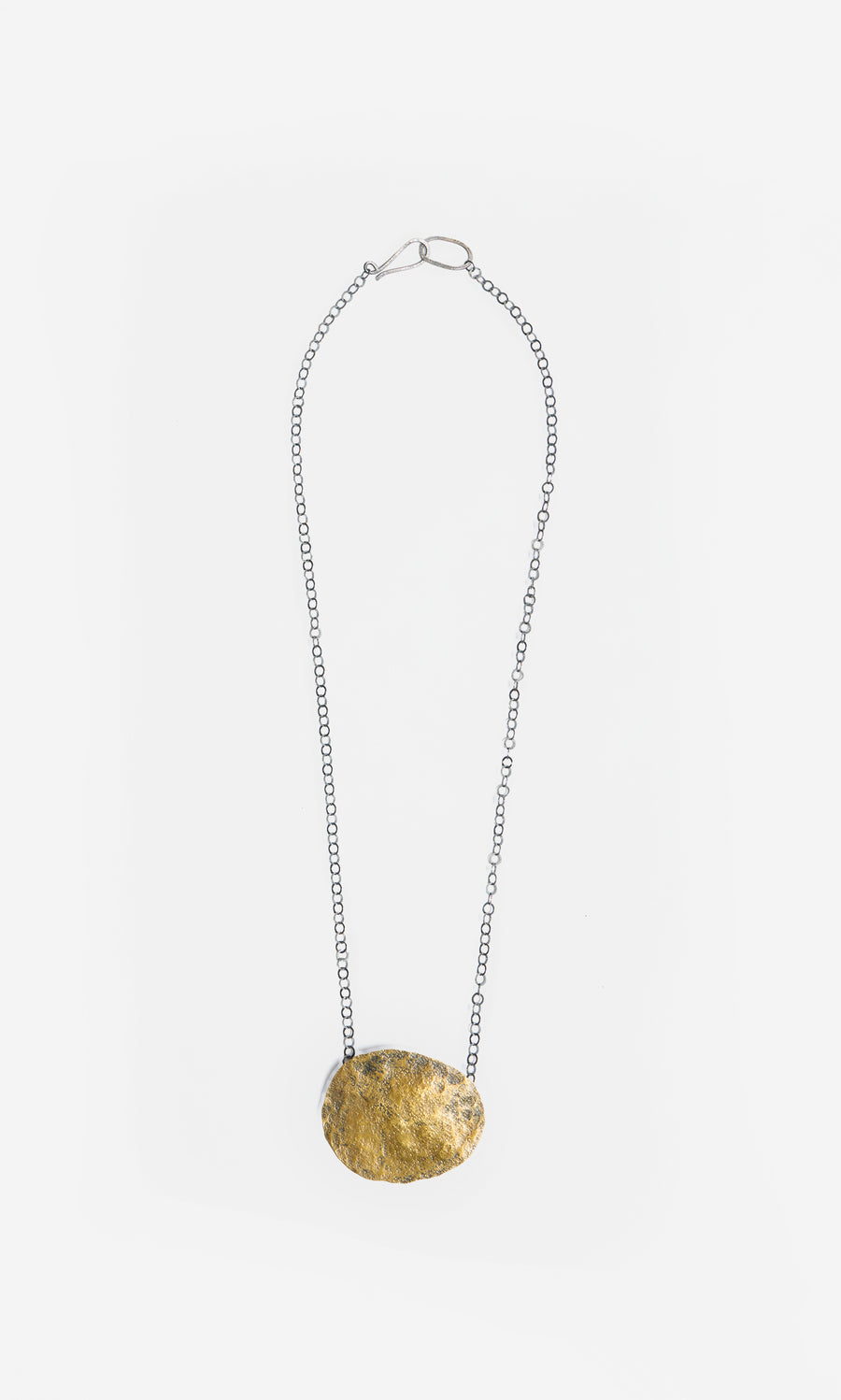 Plümo  Cressa Necklace: Artisan silver chain with a large flat gold brass pebble pendant on white background.