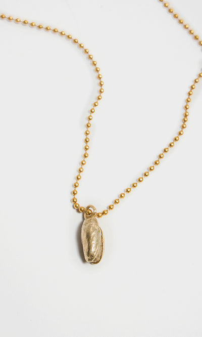Plümo  Pistachio Pendant: Gold brass ball chain necklace with a recycled brass pistachio charm on white background.