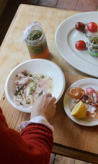 Plümo- Someone prepares a meal with onions, herbs, and lemon from Midweek Recipes By Jess Elliott Dennison.