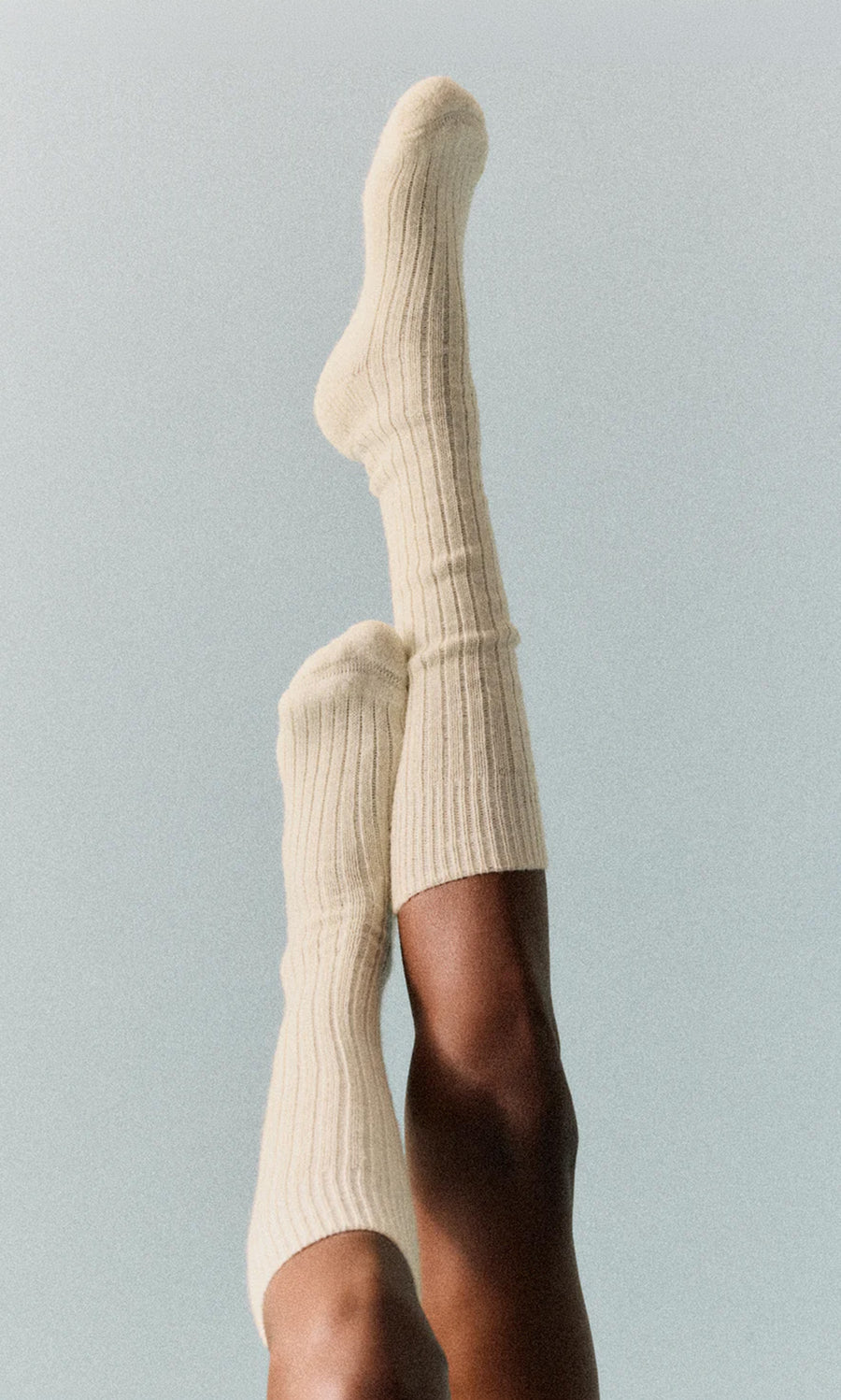 Plümo  Someone wears Clotted Cream Knee Socks with ribbed texture and cushioned sole, legs up against a light backdrop.