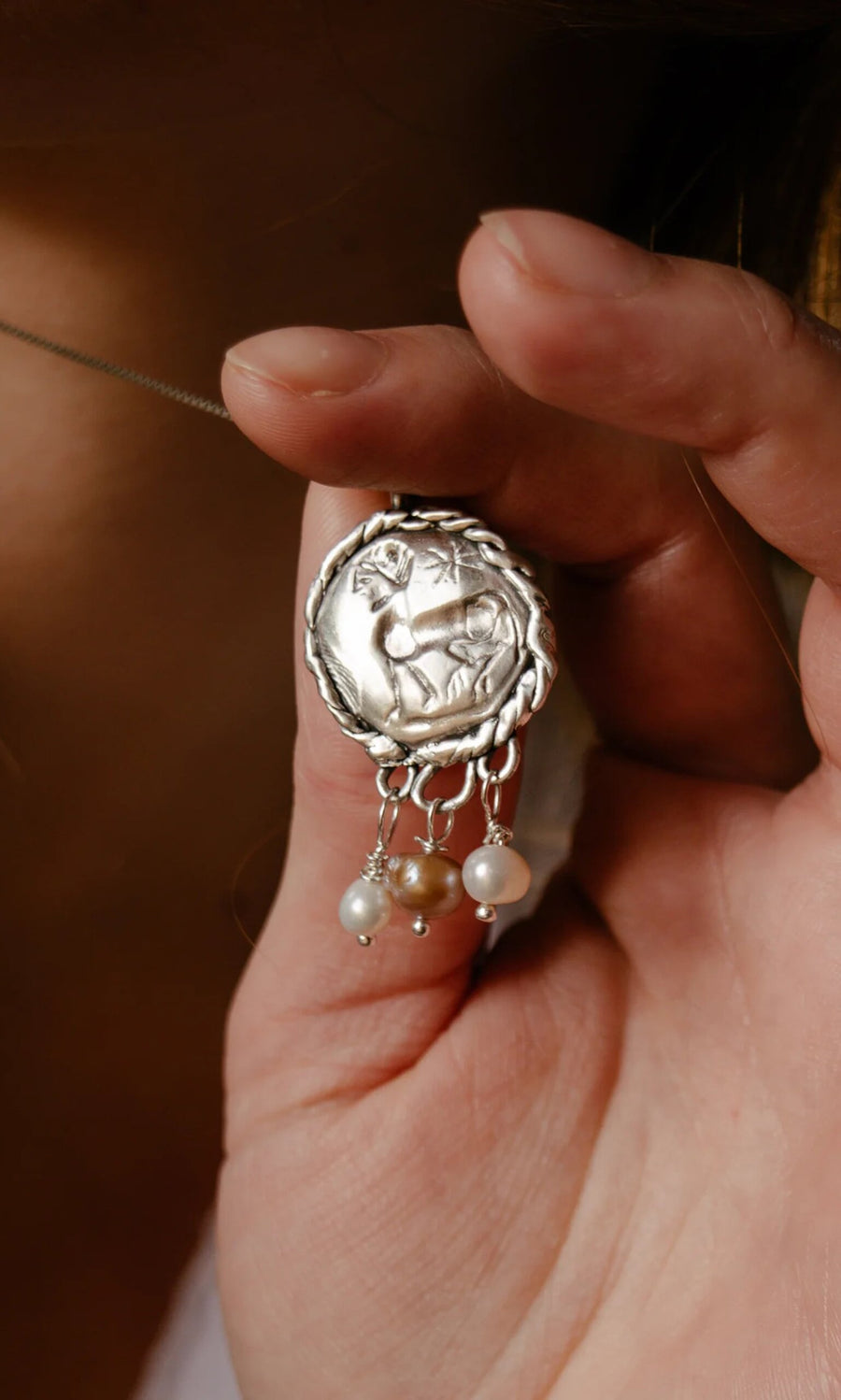 Plümo- A hand holds the Pearled Necklace, a sterling silver pendant with a deer design and three freshwater pearls.