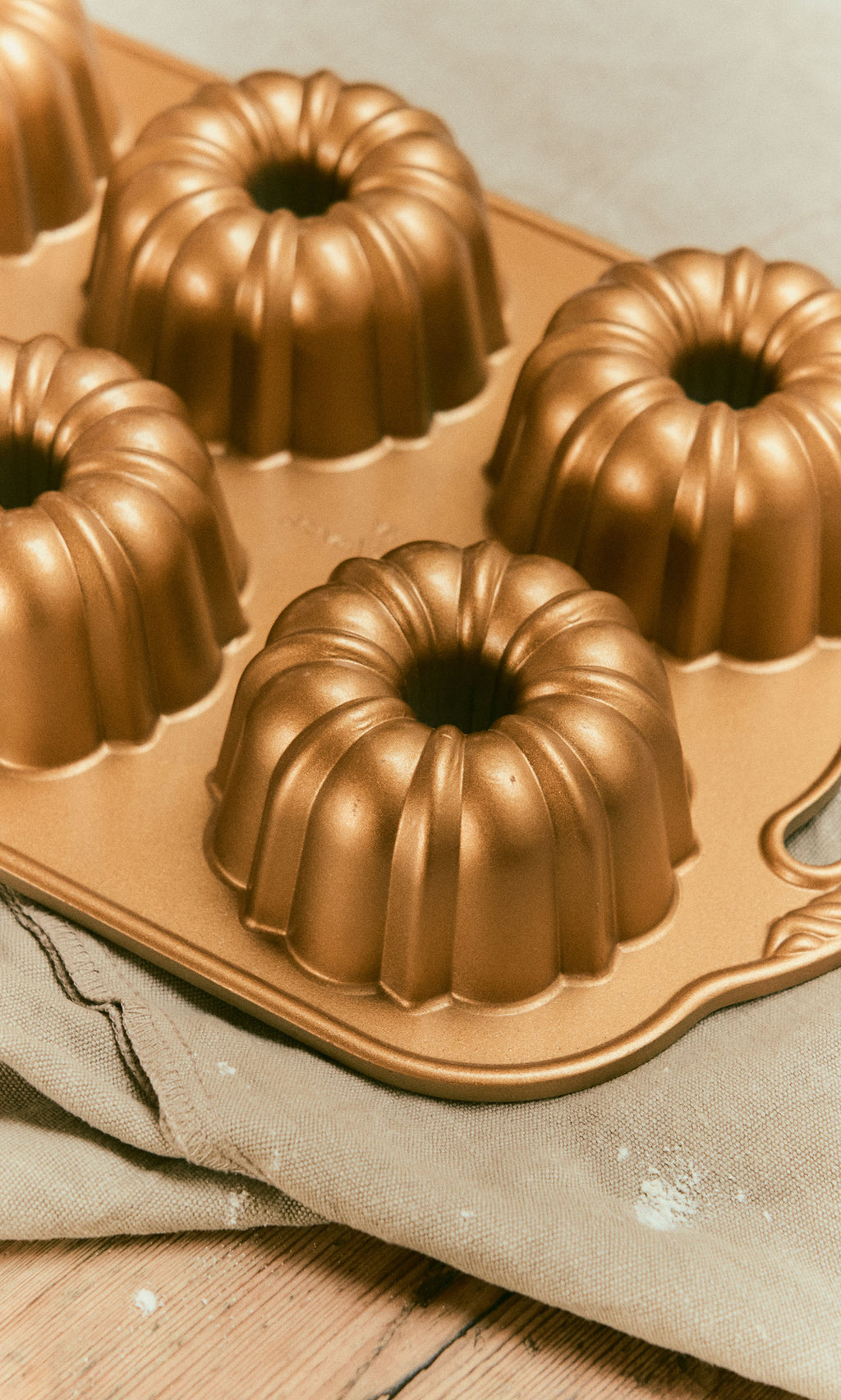 Plümo  A gold-colored Bundtlette Form mini Bundt pan with six individual fluted cake molds.