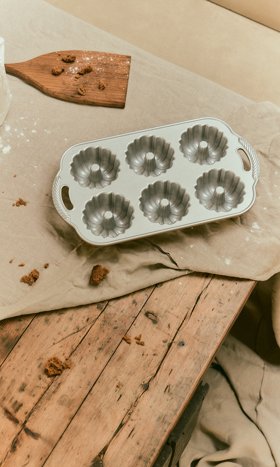 Plümo  A cast aluminium Bundtlette Form with six fluted molds resting on a cloth-covered wooden table.
