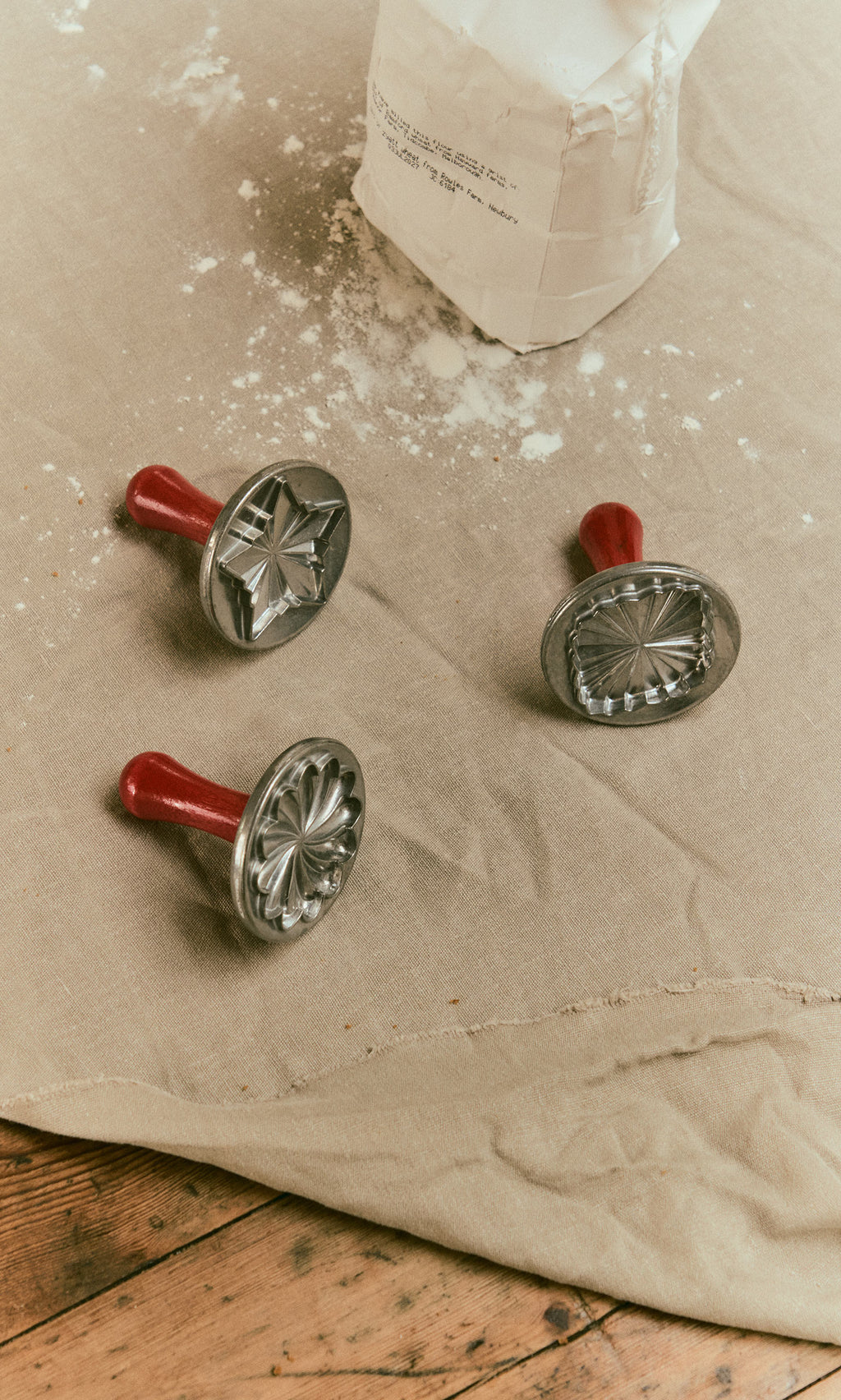 Plümo  Three cast aluminium Cookie Stamps with red handles resting on a flour-dusted cloth.