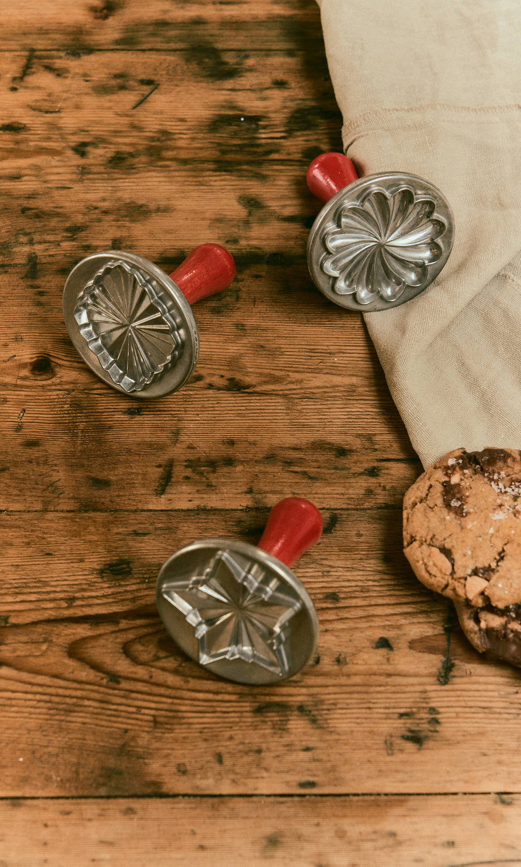 Plümo  Three Cookie Stamps with red handles and two cookies on a wooden table.