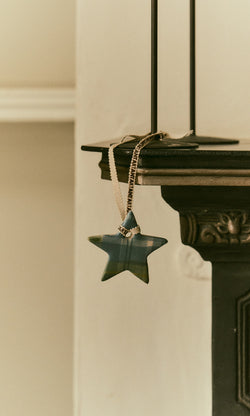 Plümo  A Tartan Star Decoration with a chain hangs from a dark ornate shelf against a light wall.