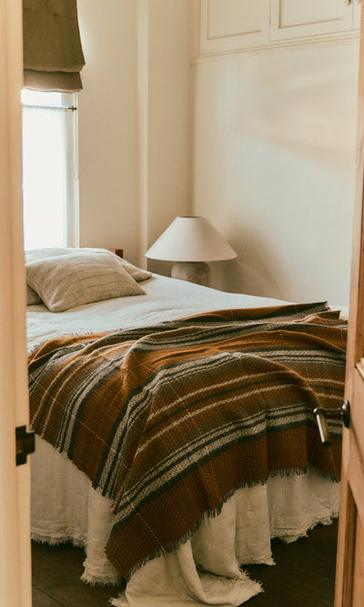 Plümo  Cozy bedroom with a bed, Random Throw, lamp, pillow, and light streaming through the curtains.