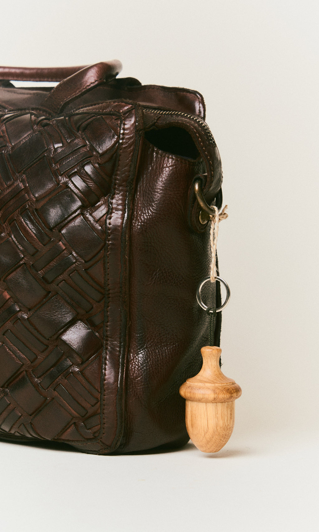 Plümo  Dark brown woven leather bag featuring an Acorn Keyring attached to a metal ring on the handle.