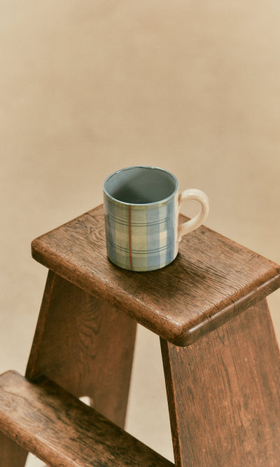 Plümo  A Blue Tartan Mug with a blue and green pattern sitting on a small wooden stool.