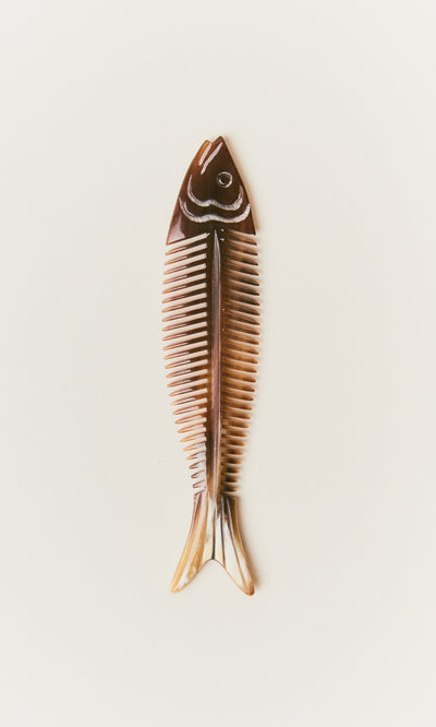 Plümo  The Sardine Comb, brown with white highlights, features a fishbone shape and rests on a plain light background.