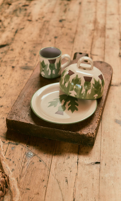 Plümo  Thistle Cheese Dome made from sustainable British clay with green tree pattern on a rustic wooden table.