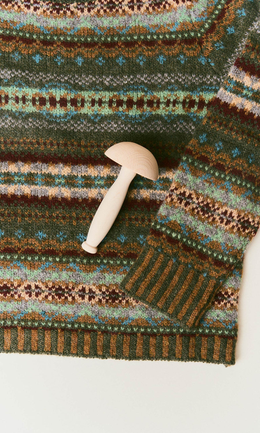 Plümo  A wooden Darning Mushroom resting on a patterned green knit sweater.